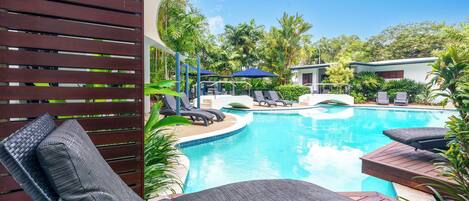 A pool area with lounge chairs and umbrellas, surrounded by lush greenery.