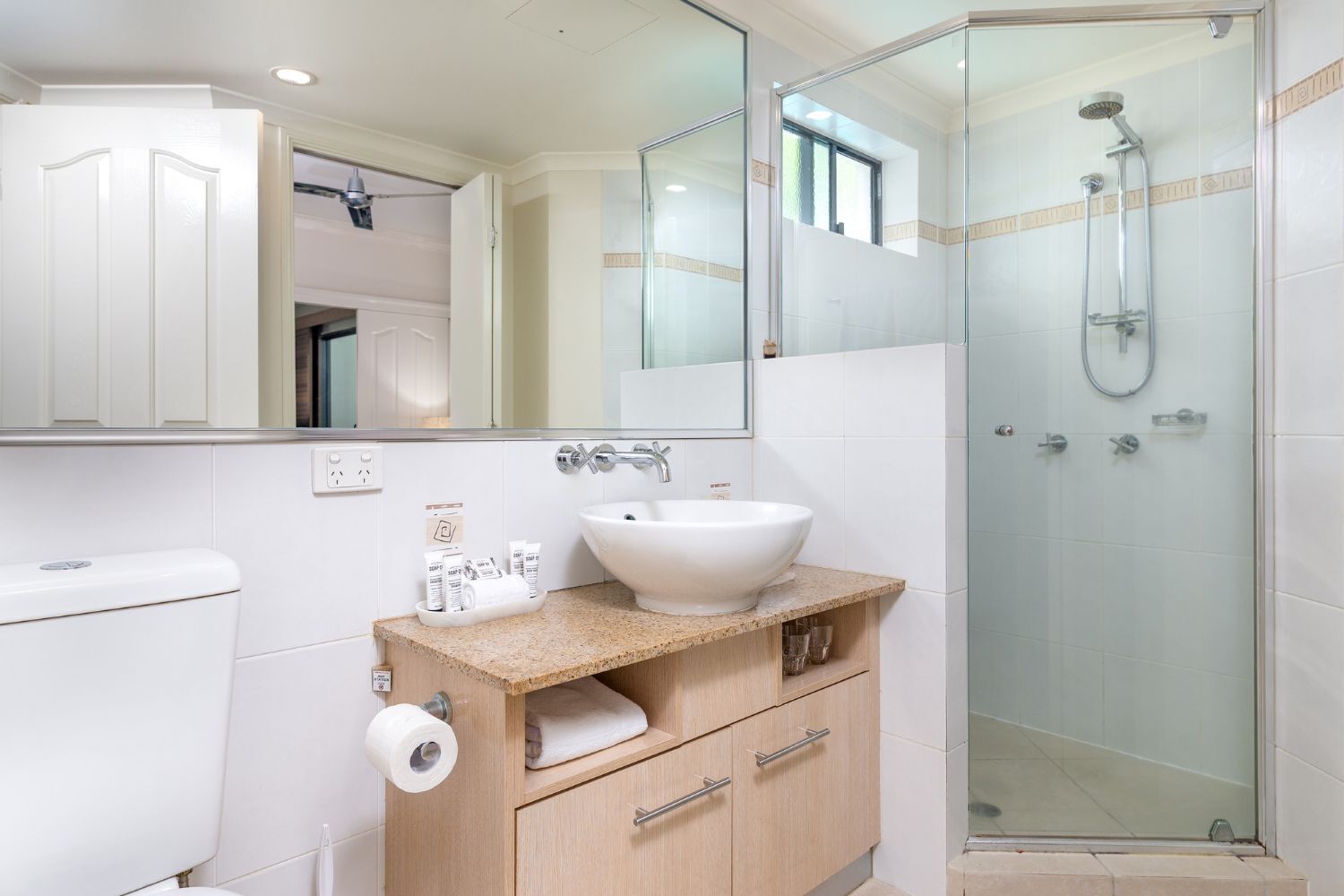 A modern bathroom with a white toilet, a sink with a beige countertop, a mirror, and a glass-enclosed shower.