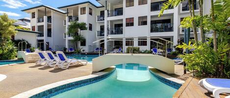 Um hotel com piscina, espreguiçadeiras e um edifício de vários andares.