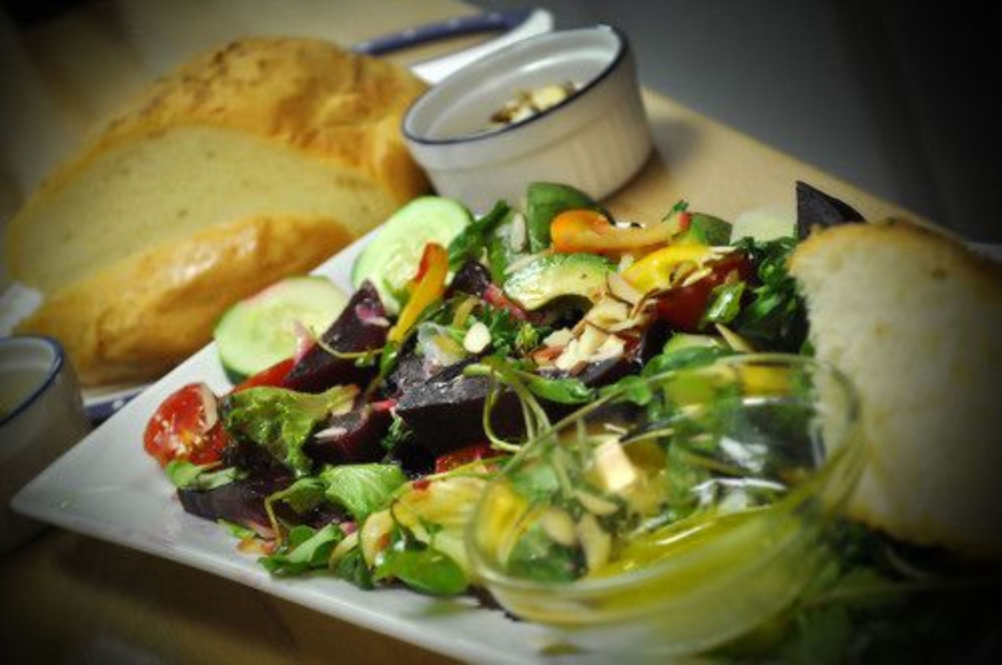 A plate of mixed greens salad with a slice of bread and a small bowl of dressing.