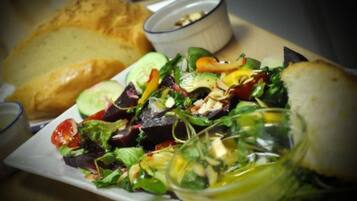 A plate of mixed greens salad with a slice of bread and a small bowl of dressing.