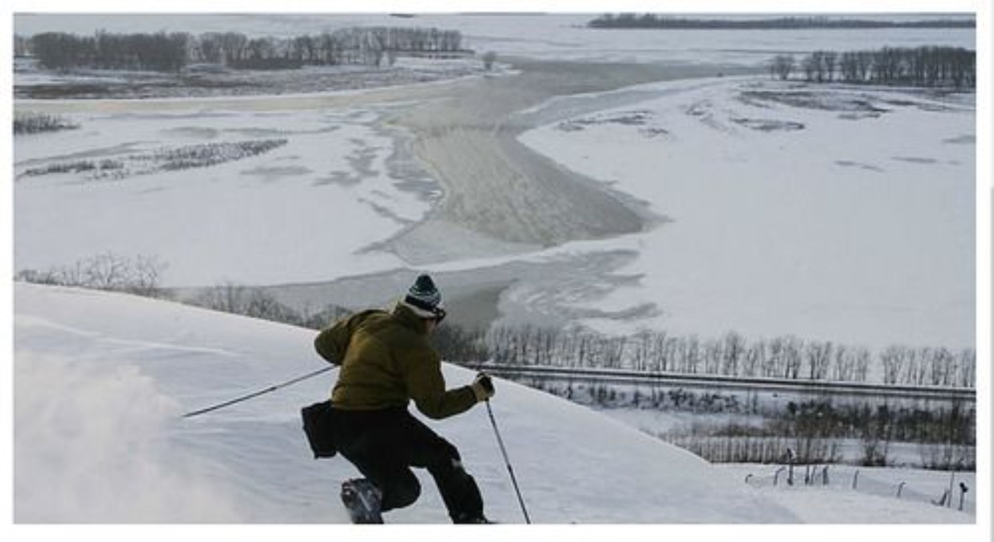 Una persona esquiando en una ladera nevada, con un río al fondo.