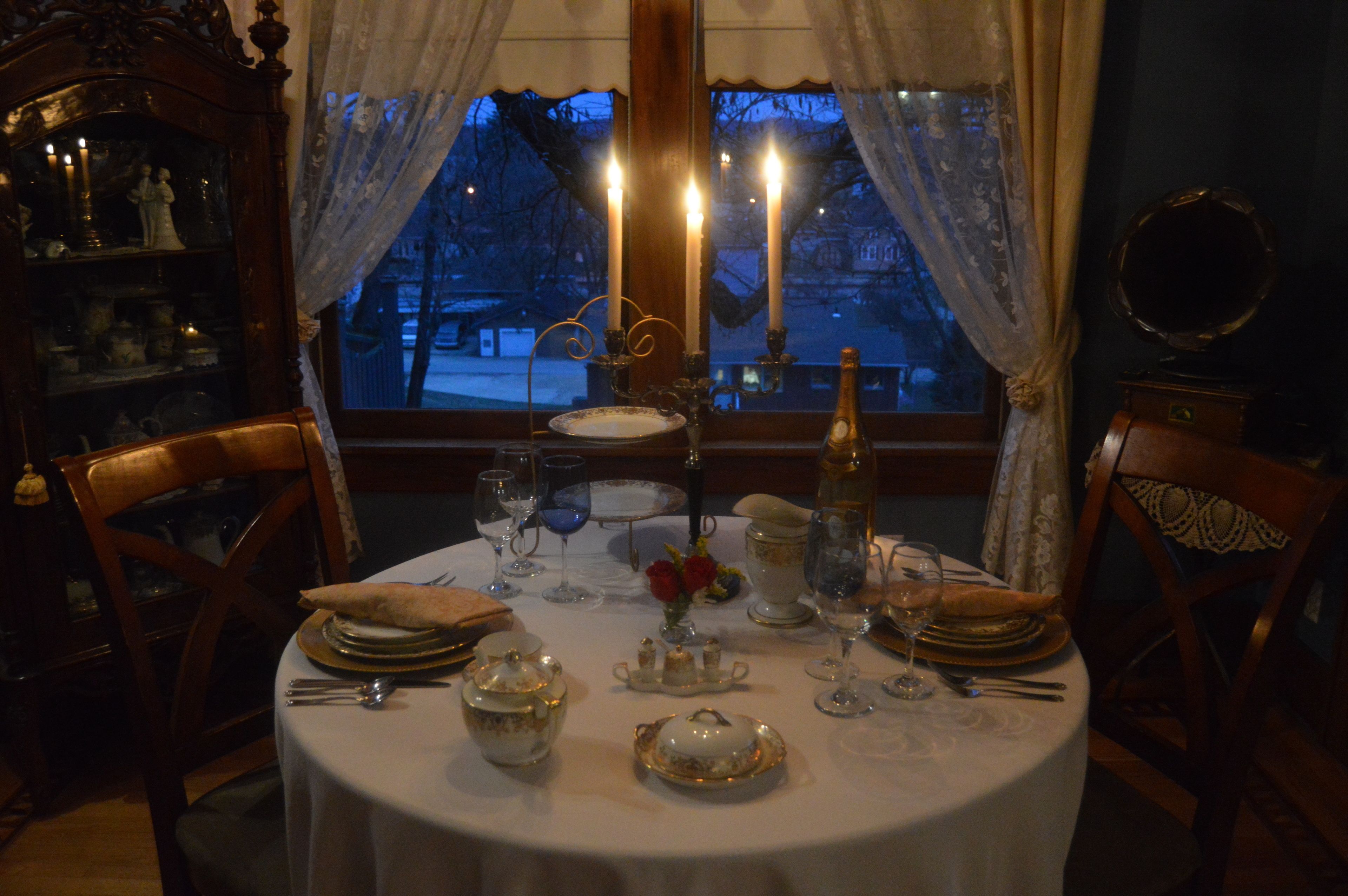 A dining table set for four with candles, plates, glasses, and a vase of flowers.
