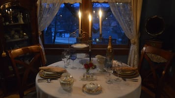 A dining table set for four with candles, plates, glasses, and a vase of flowers.