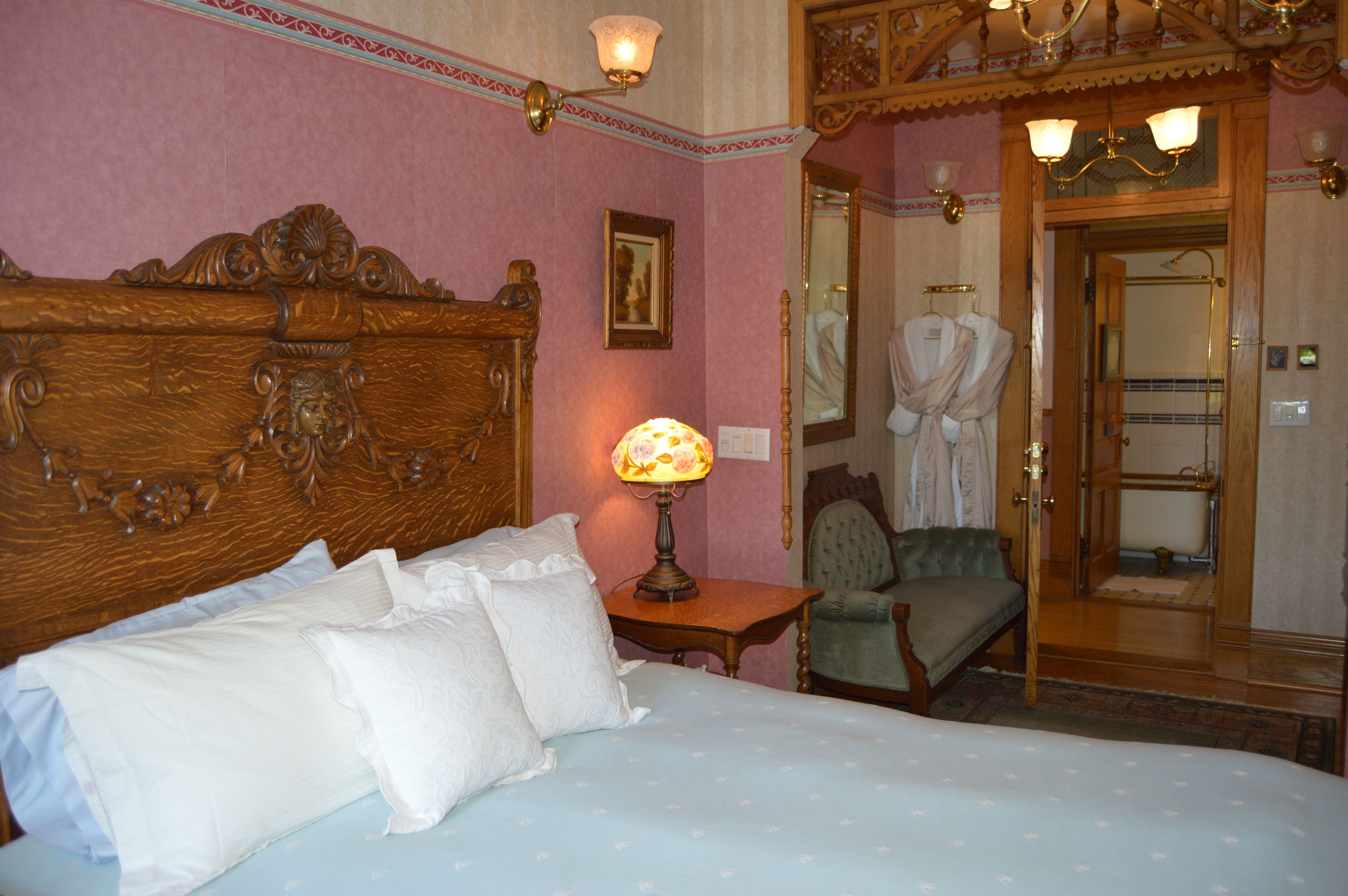 A bedroom with a large wooden headboard, a bedside table with a lamp, a chair, and a mirror.