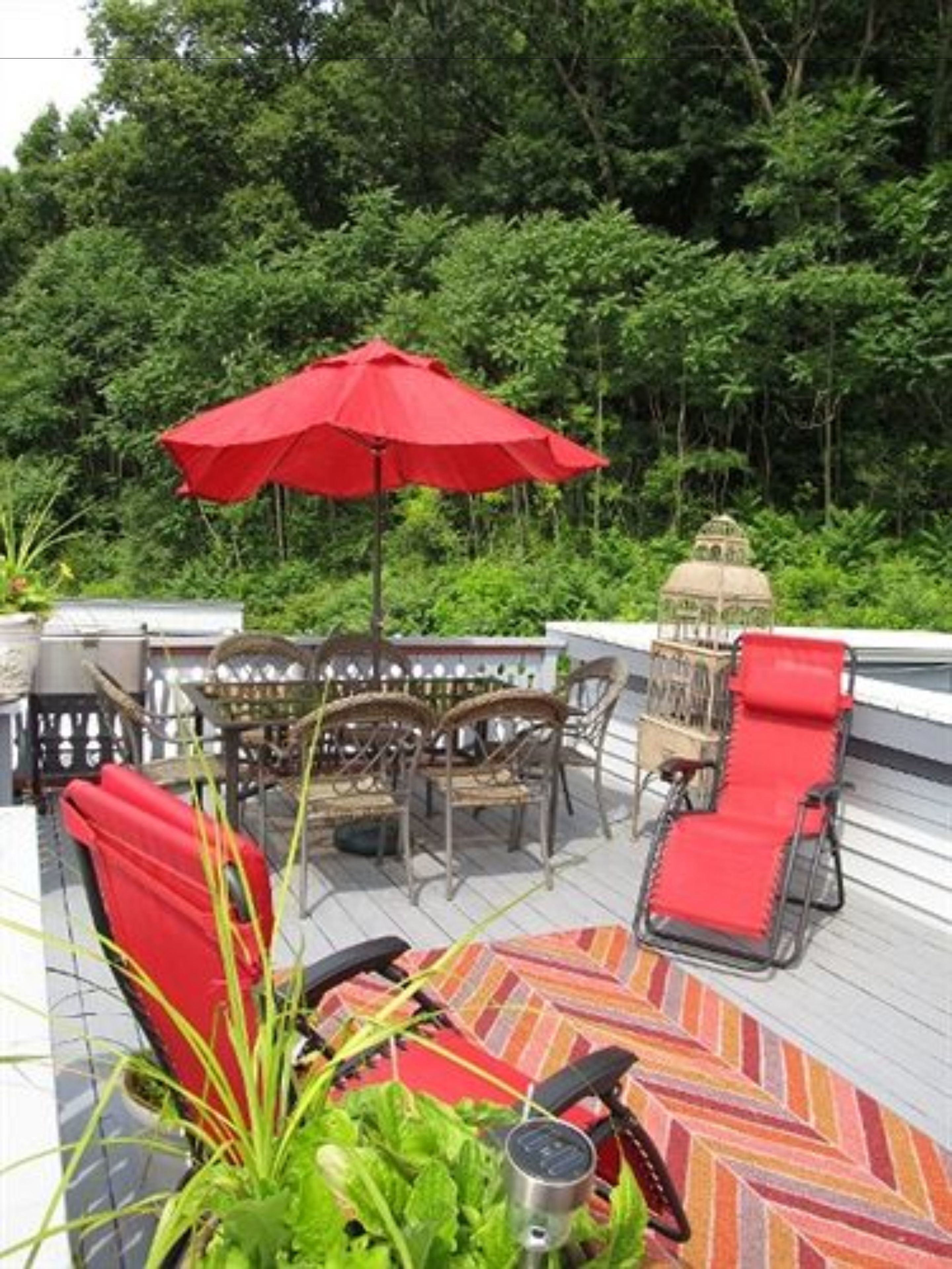 An outdoor deck with a dining set, a red umbrella, and lounge chairs.