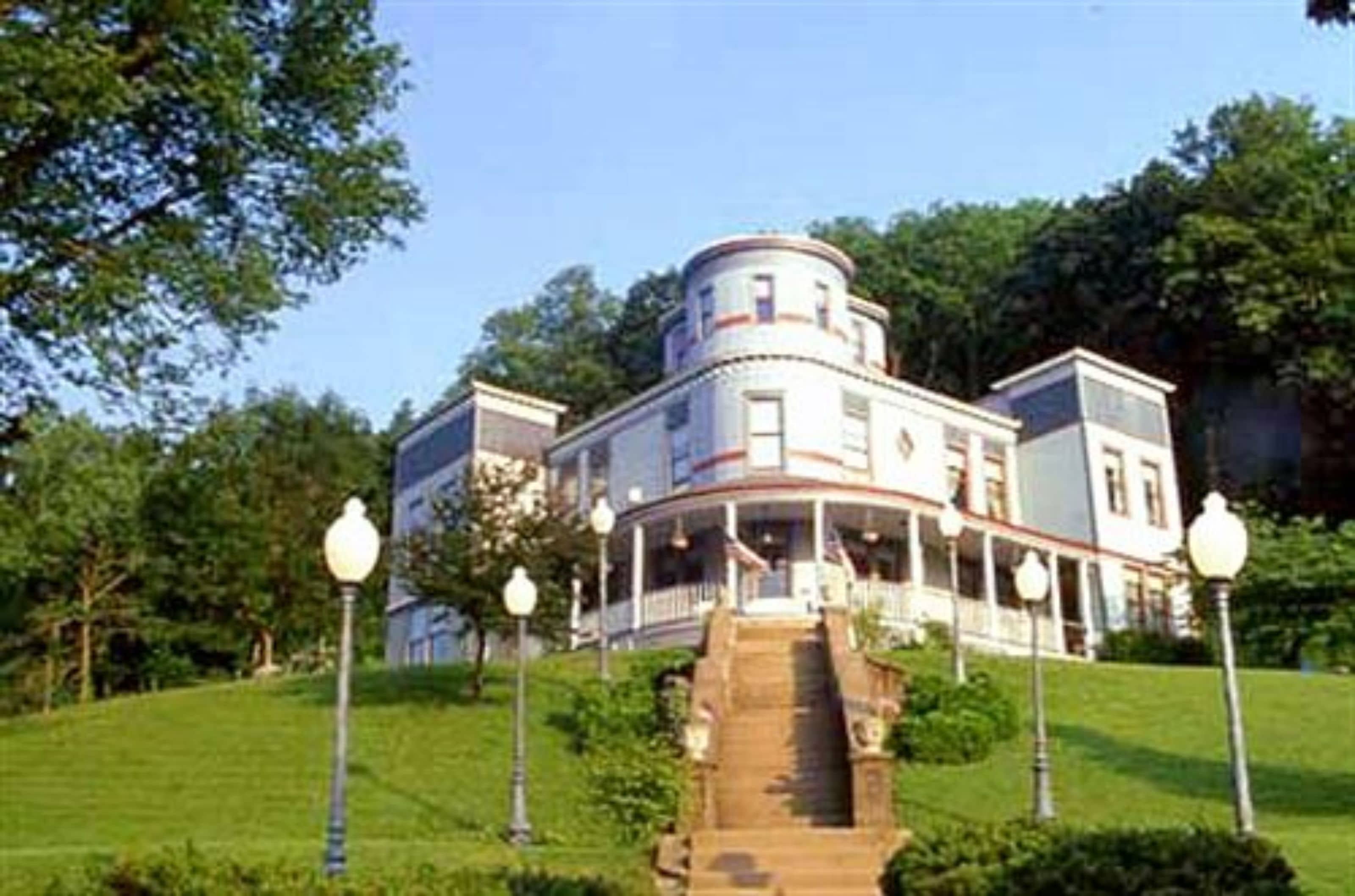 A large, historic building with a central tower, multiple stories, and a covered front porch.