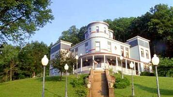 A large, historic building with a central tower, multiple stories, and a covered front porch.