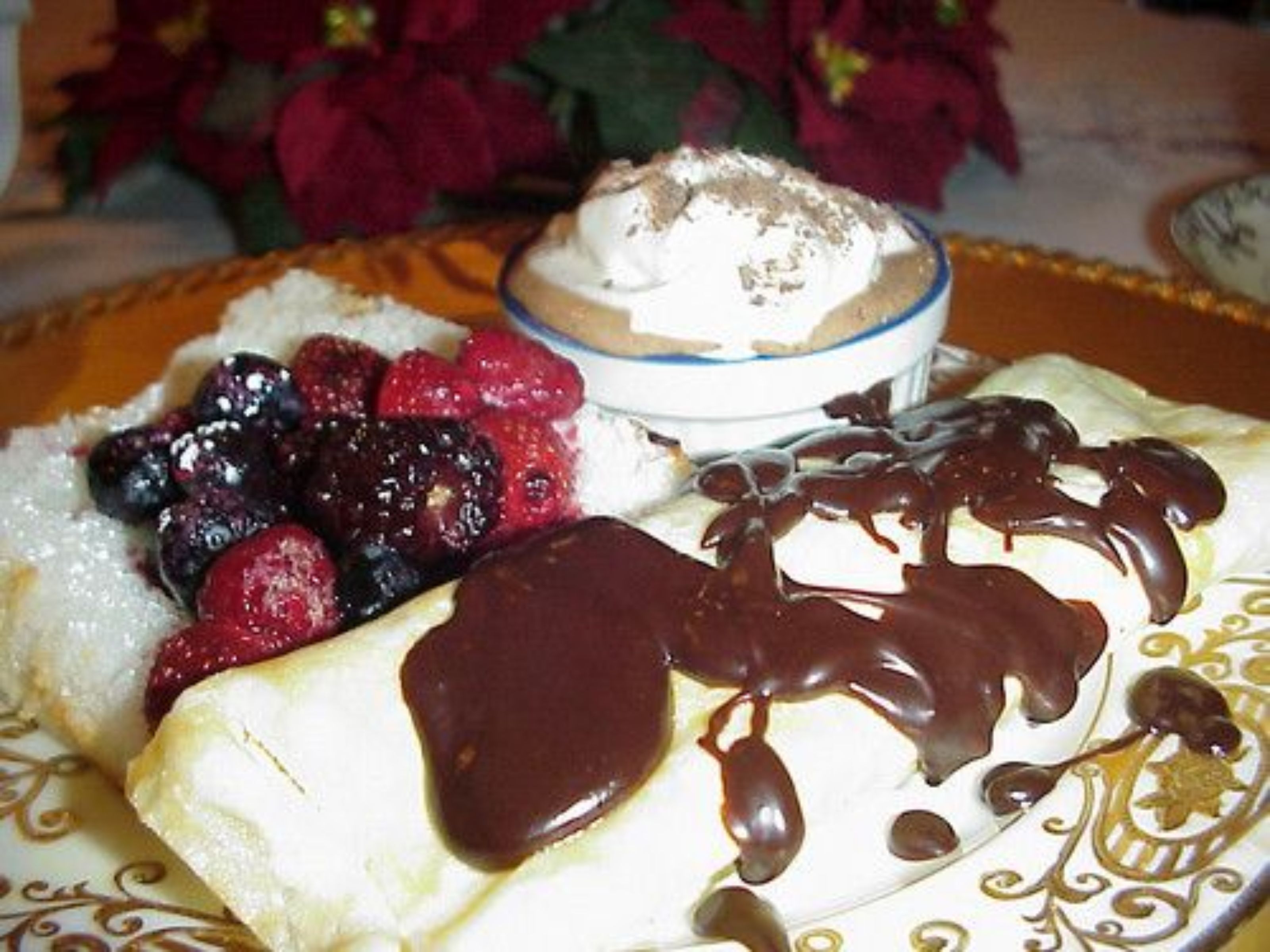 Un plato de postre con goteo de chocolate, frutos rojos y crema batida.