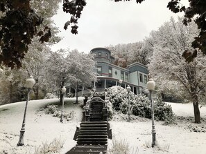 Un sendero cubierto de nieve que conduce a una casa histórica con porche y escaleras.