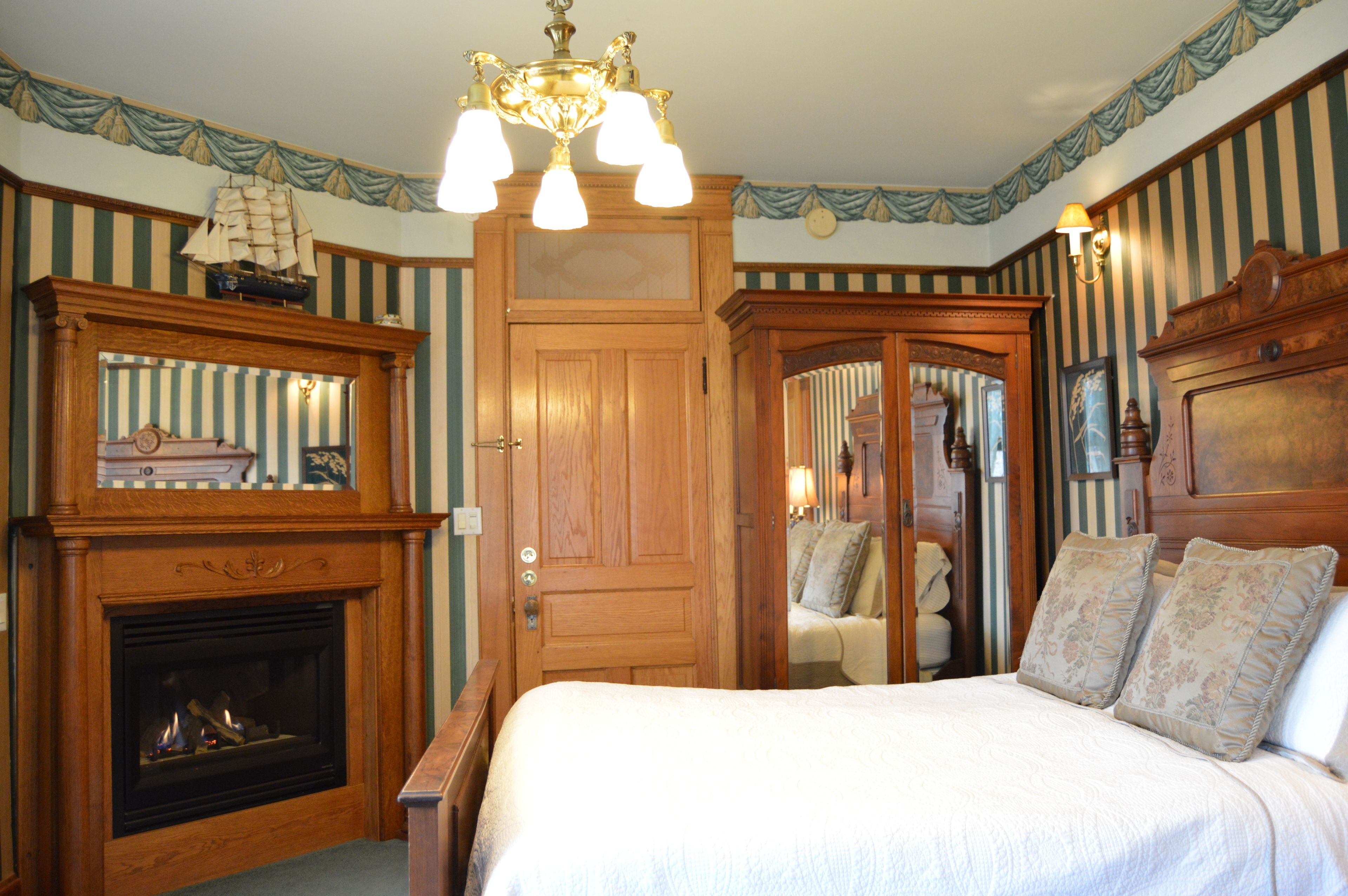 Una habitación con chimenea, una cama con almohadones florales y un modelo de barco en la repisa.