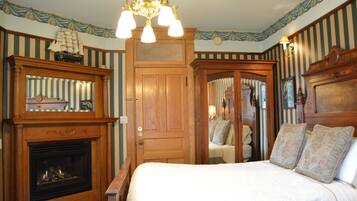 Una habitación con chimenea, una cama con almohadones florales y un modelo de barco en la repisa.