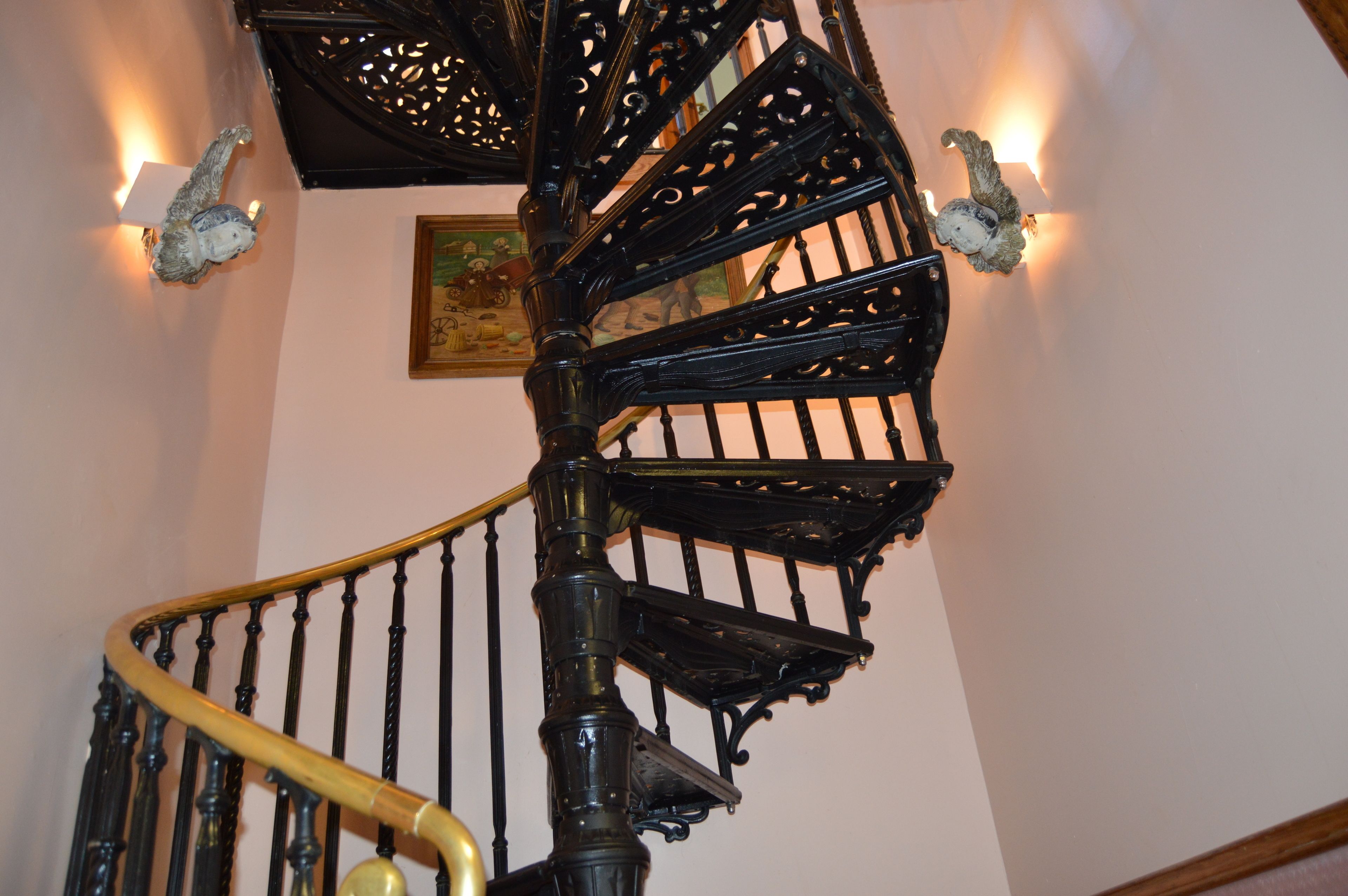 Una escalera de caracol con barandillas negras ornamentadas y un pasamanos de madera.