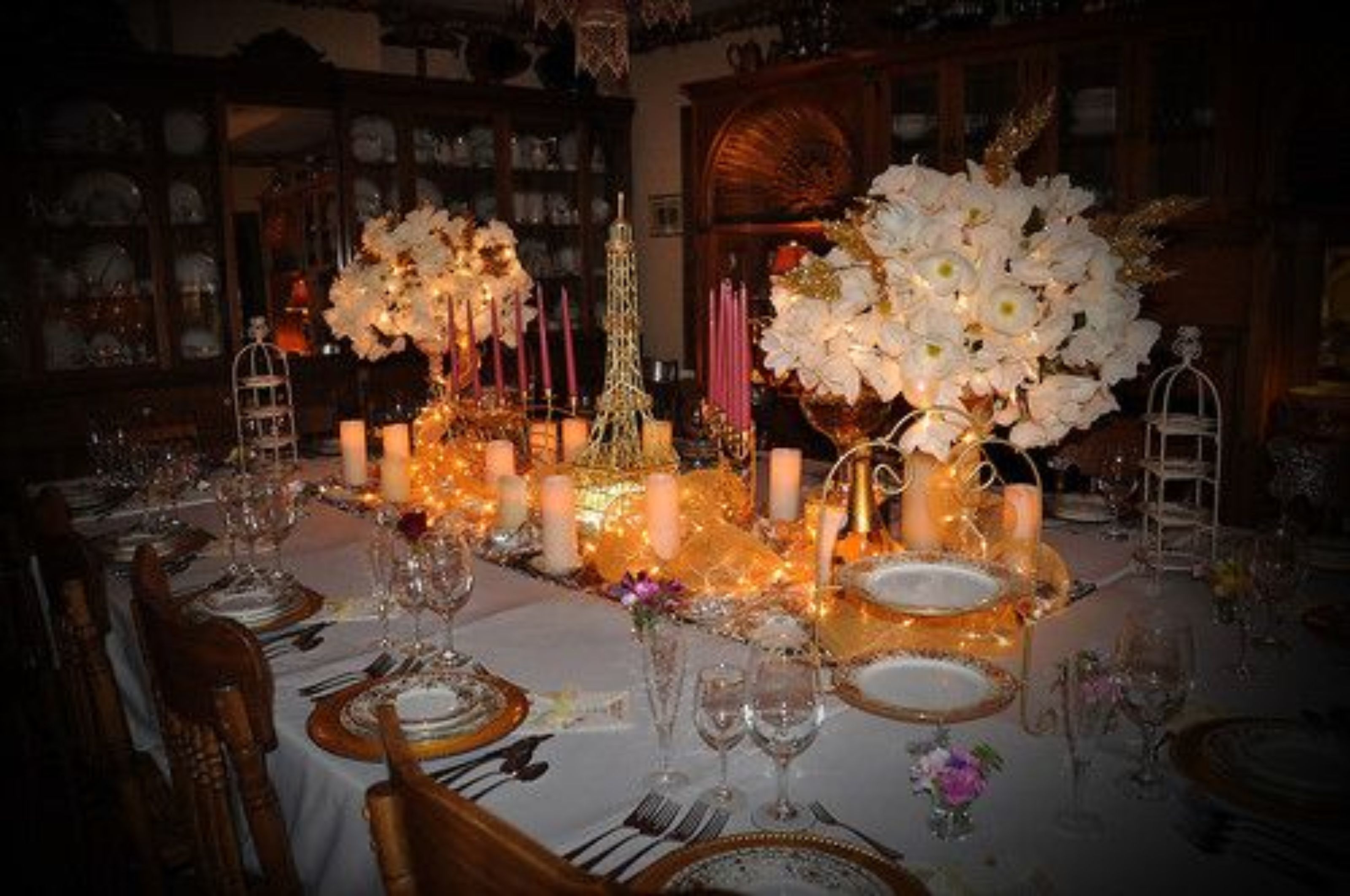 A formal dining table set with candles, flowers, and a decorative Eiffel Tower centerpiece.