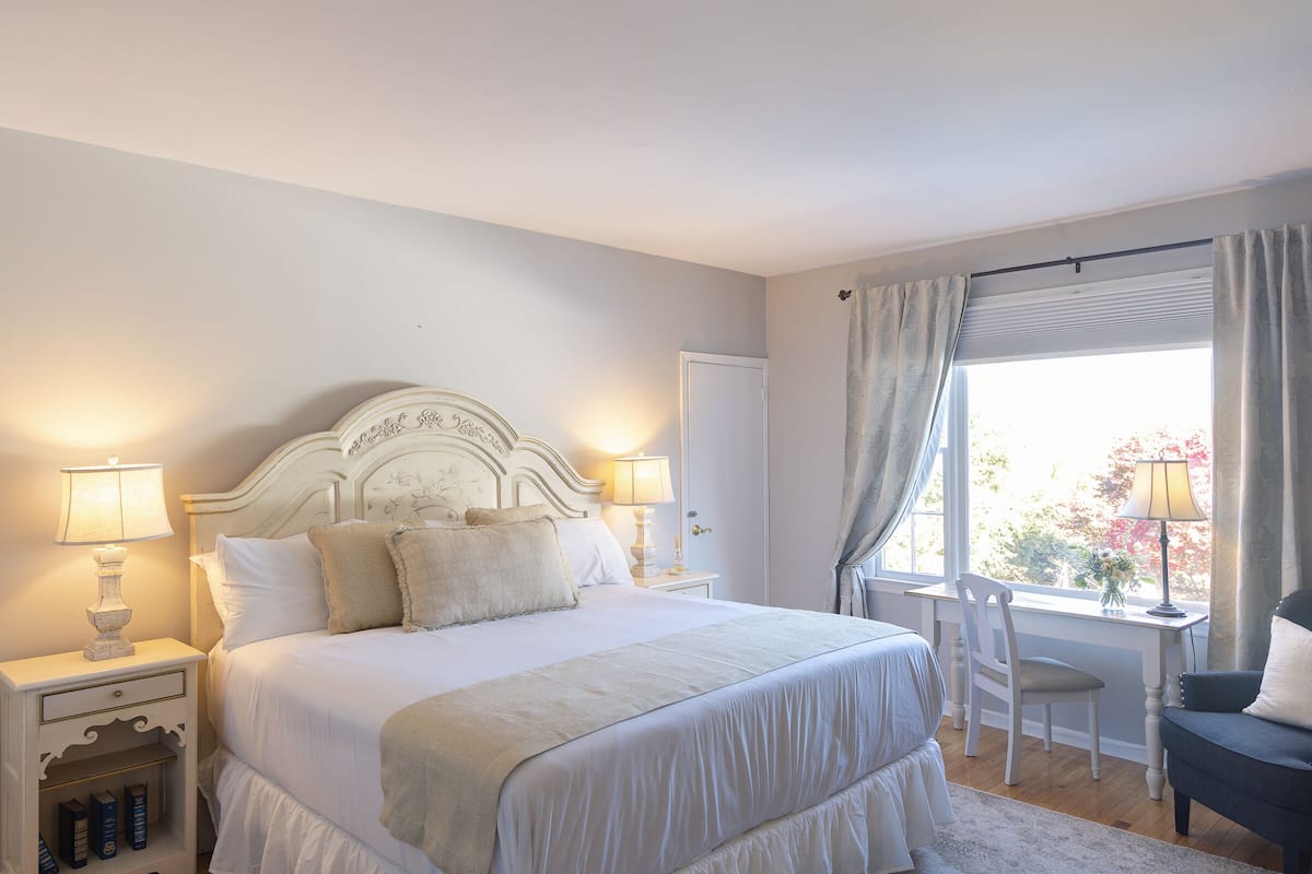 A bedroom with a large bed, bedside tables with lamps, a chair, and a window with curtains.