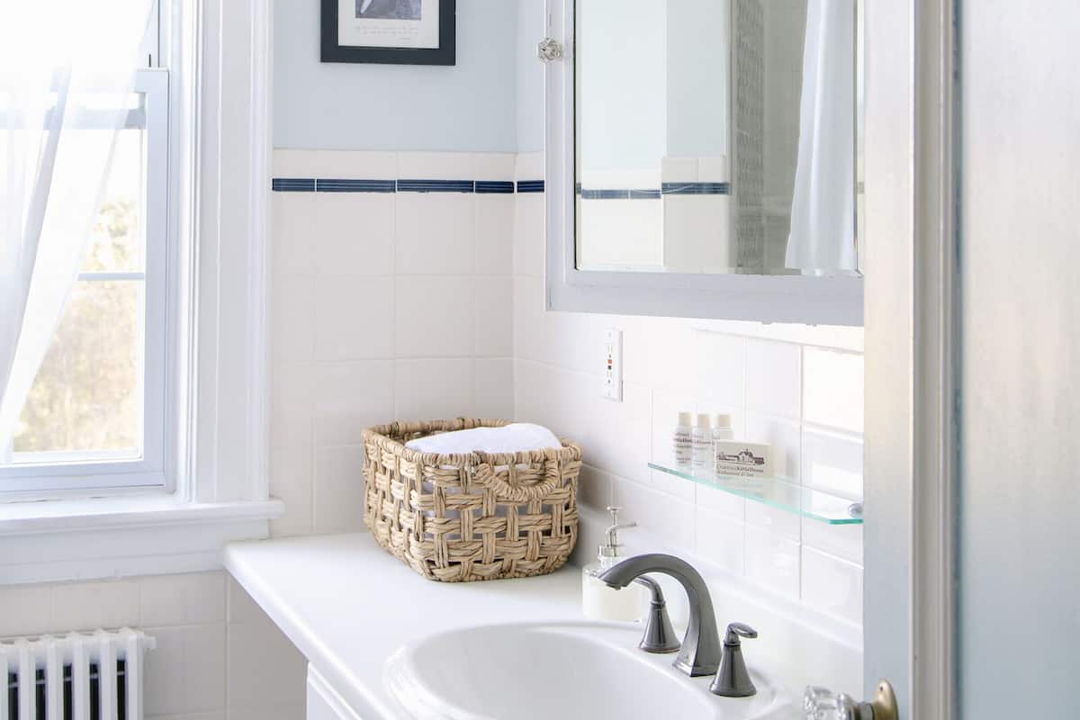 A bathroom with a white sink, a large mirror, a wicker basket, and a framed picture on the wall.