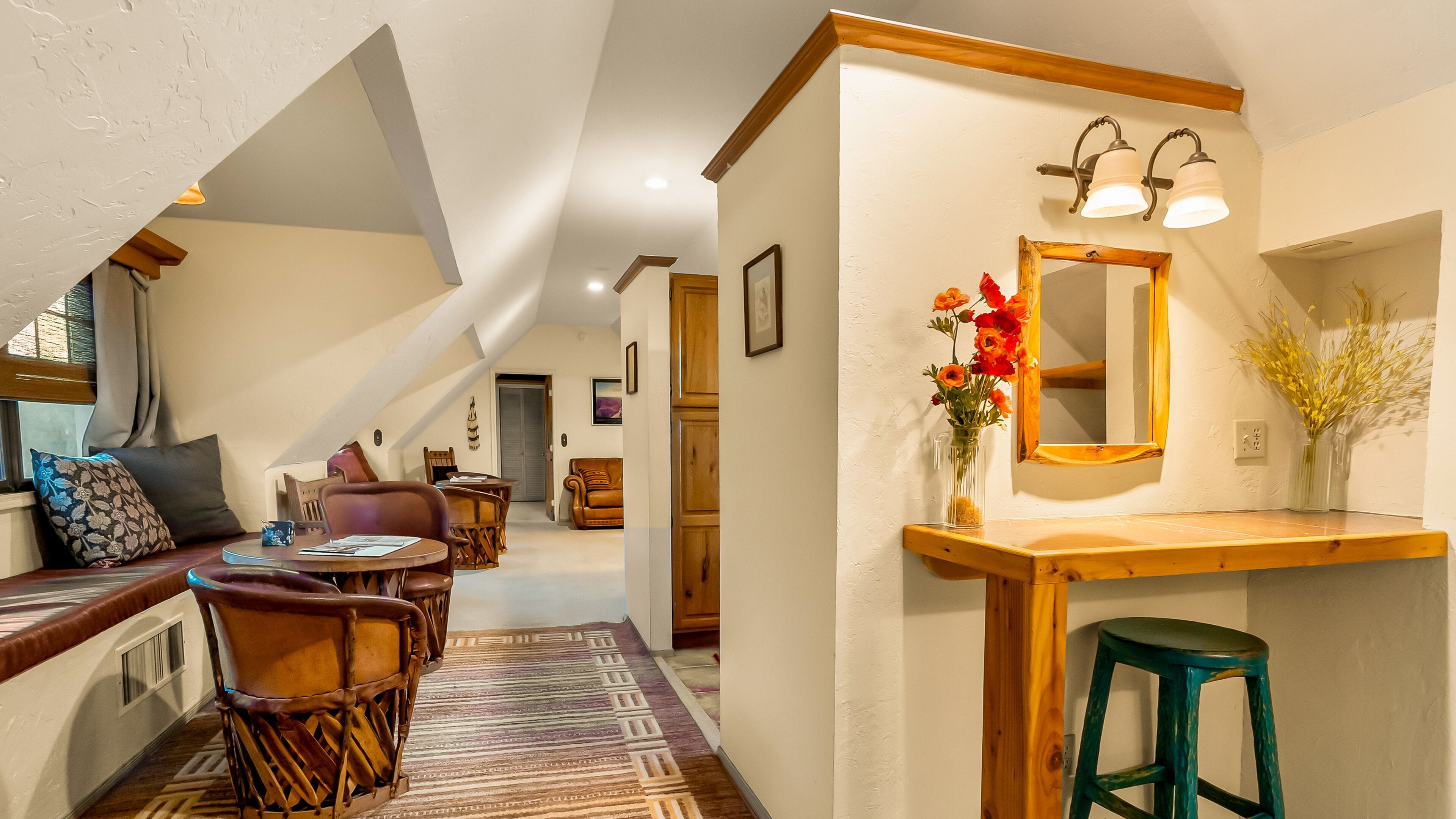 A cozy, well-lit room with a wooden bench, a dining table, and a mirror above a sink.