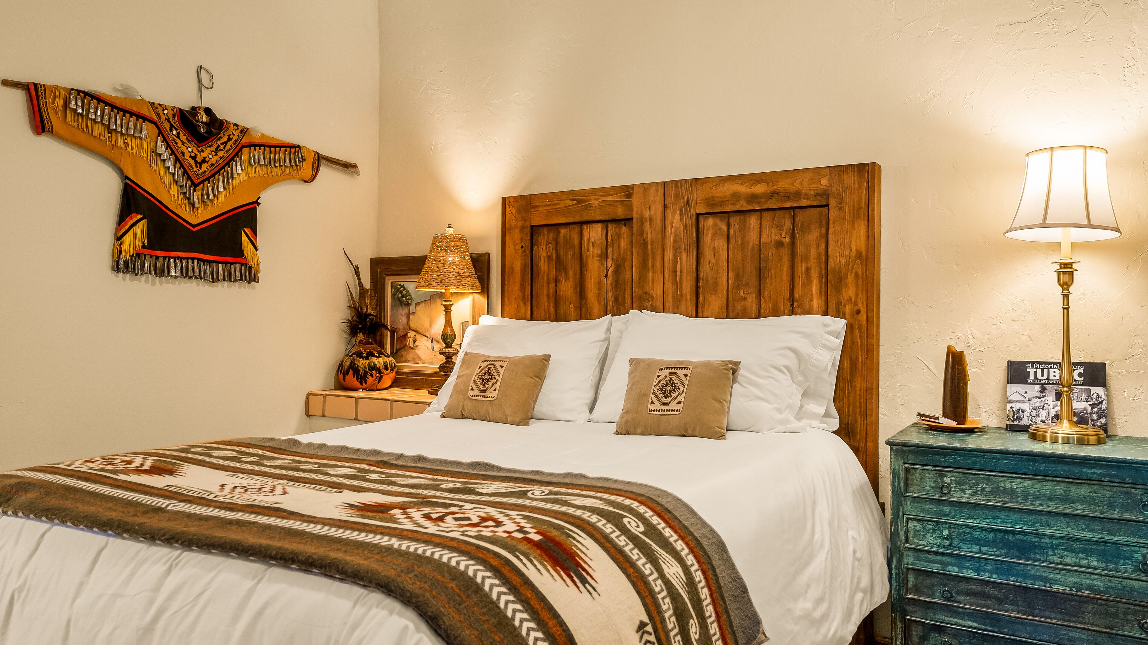 Una cama con sábanas blancas, cabecera de madera y manta estampada.