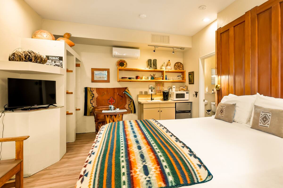 A compact hotel room with a bed, a TV, a kitchenette, and a bathroom.