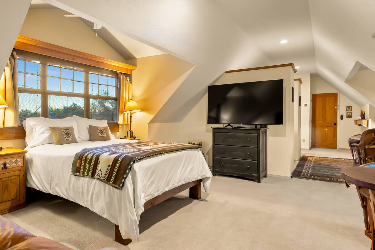 A bedroom with a large bed, a TV, a dresser, and a window with curtains.