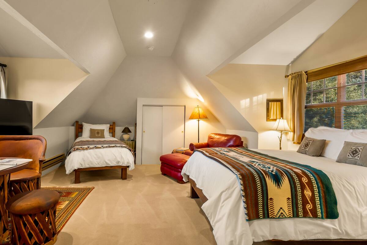 A cozy attic bedroom with a TV, two beds, a desk, and a chair.