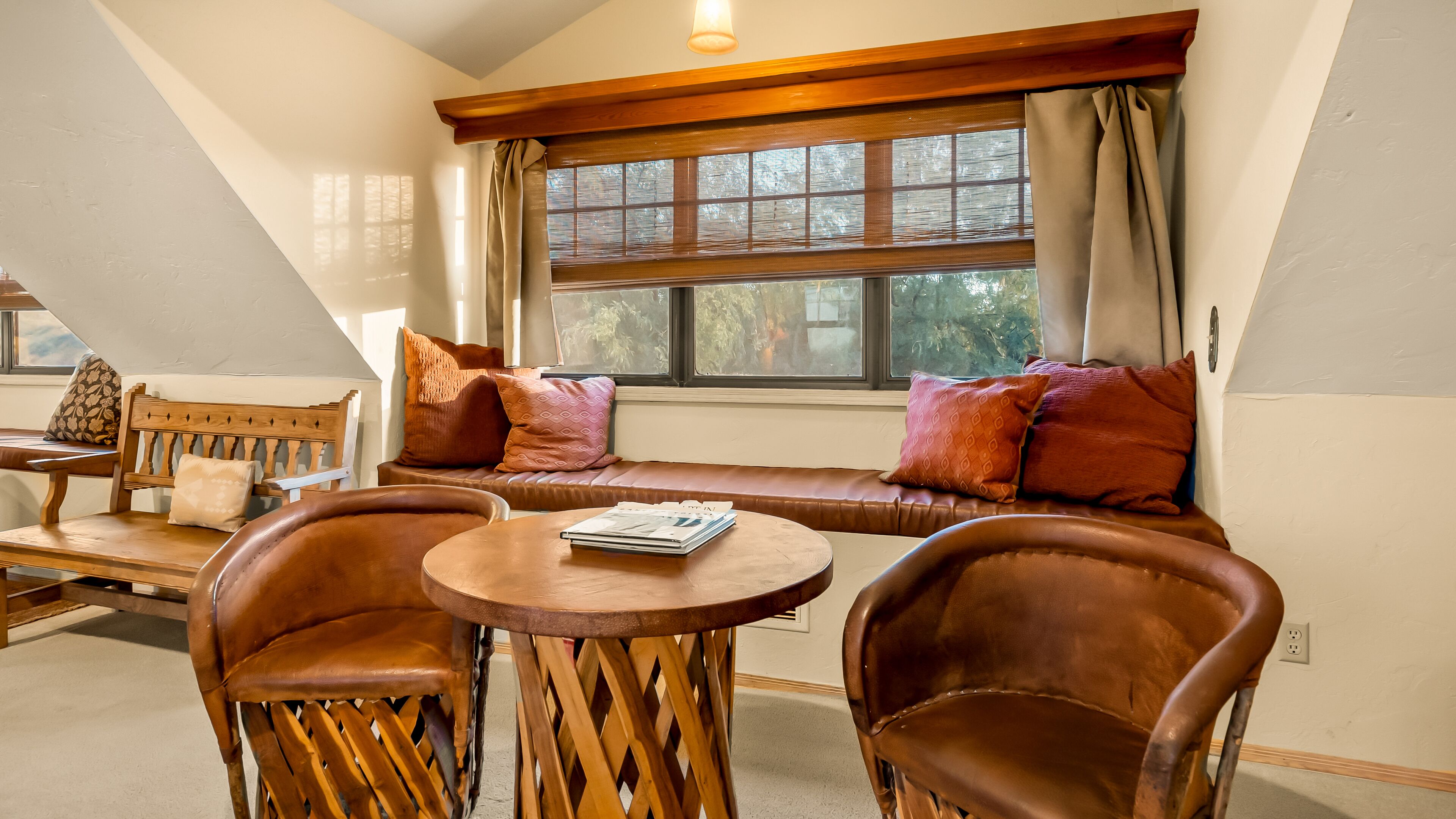 A cozy seating area with a bench and two chairs, a table with magazines, and a large window with curtains.