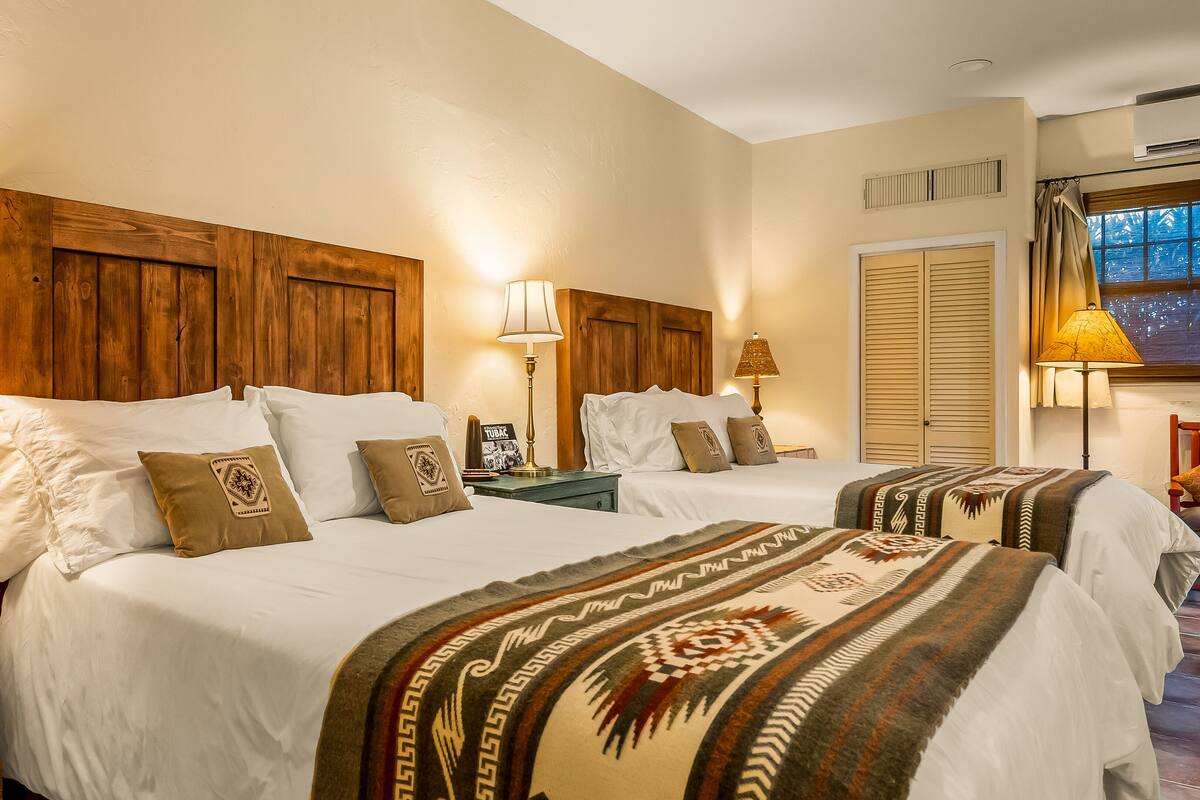 A hotel room with two beds, wooden headboards, and a view of the city through a window.