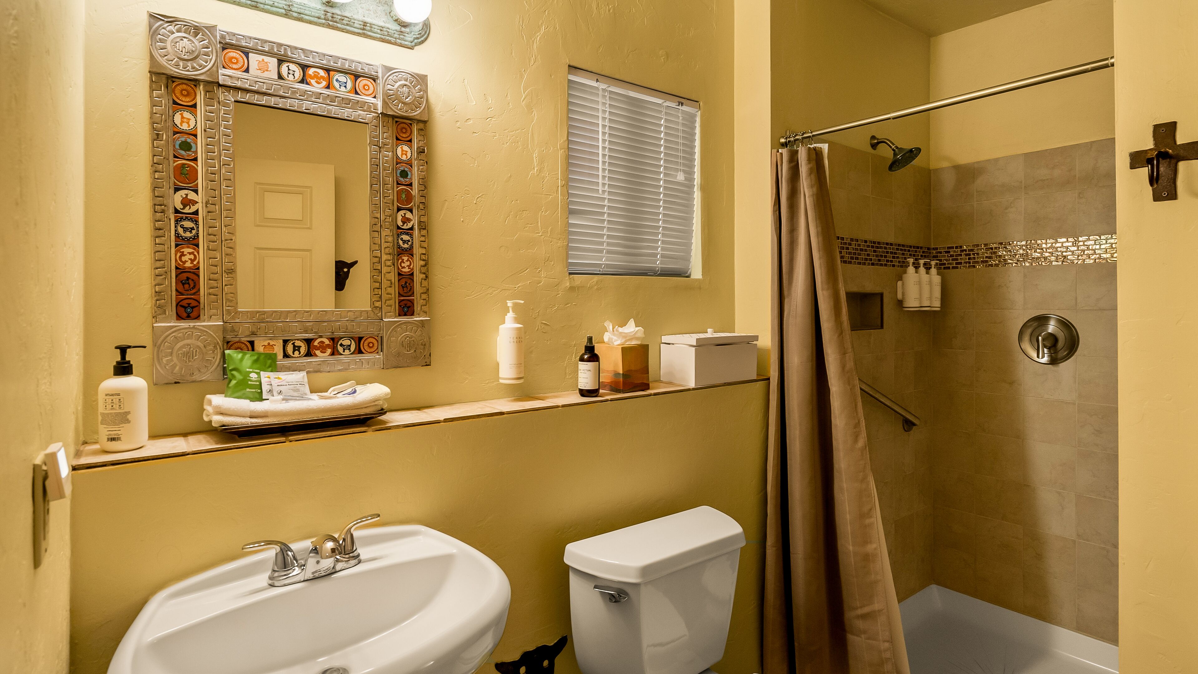 Une salle de bain équipée d’un lavabo, de toilettes, d’une douche et d’un miroir agrémenté de carreaux décoratifs.