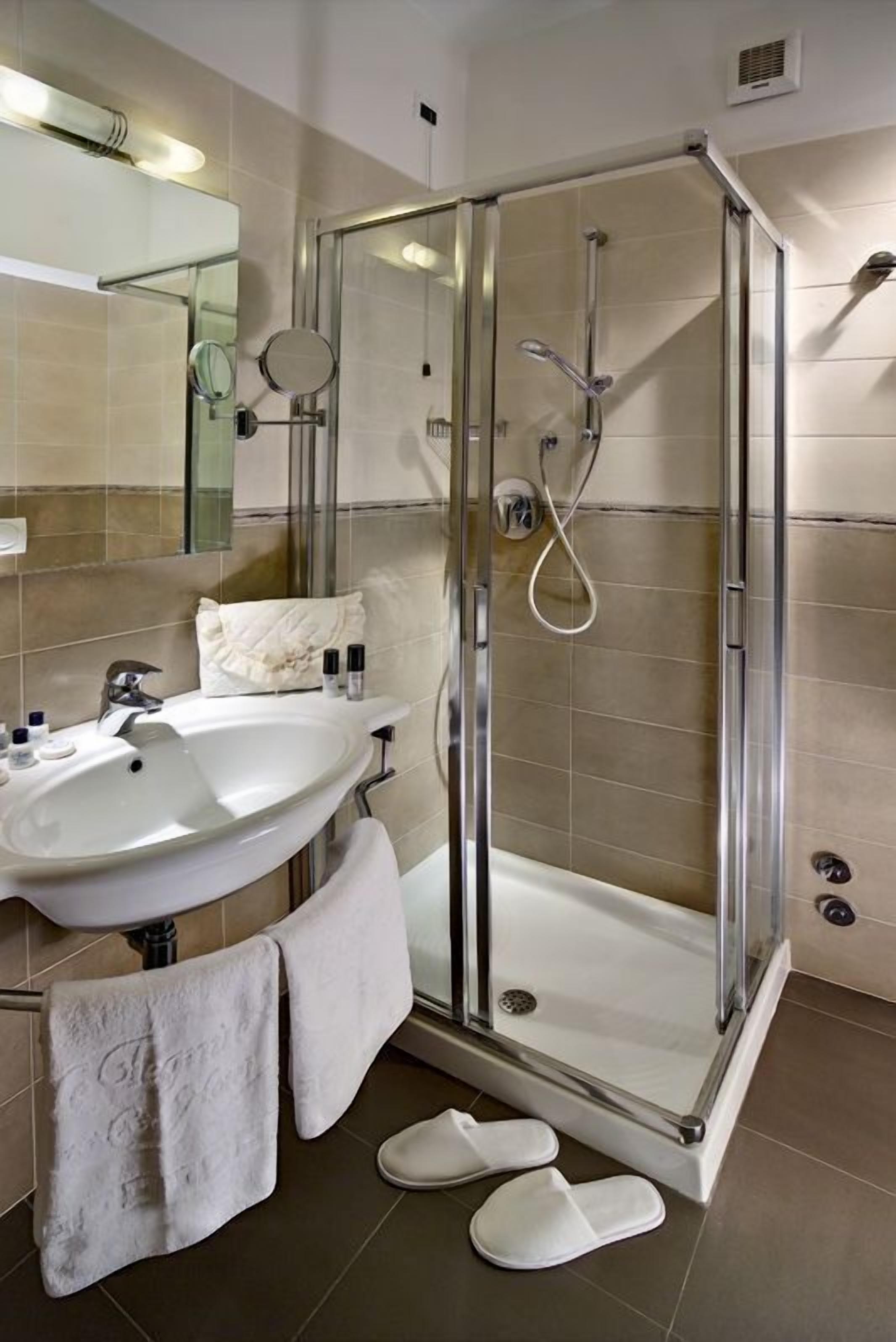 Un baño moderno con ducha envuelta en vidrio, lavamanos y espejo.