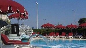 A swimming pool with red umbrellas, lounge chairs, and a clear blue sky. - Hotel Le Tegnue (Chioggia)