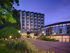 A hotel with a modern design, featuring a central entrance with a glass facade, a landscaped garden with roses, and a brick pathway leading to the entrance. - Hotel Le Tegnue (Chioggia)
