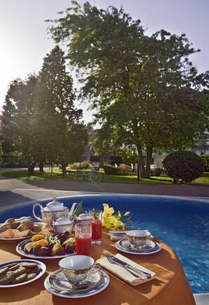 A dining table set with breakfast items by a poolside, surrounded by trees and a bicycle in the background. - Hotel Le Tegnue (Chioggia)