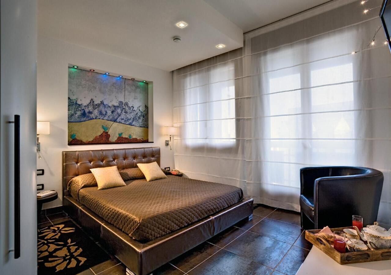 Ein modernes Hotelzimmer mit einem großen Bett, einem Gemälde an der Wand, einer Essecke mit einer Platte mit Speisen und einem Fenster mit leichtem Vorhang.