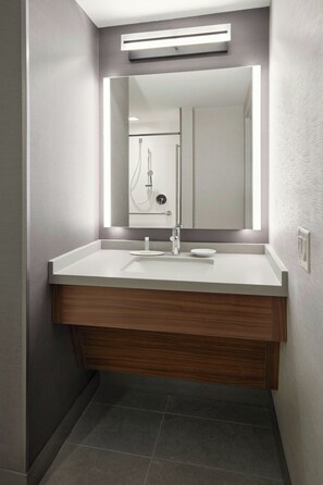 A modern bathroom with a white vanity, a mirror, and a shower visible in the background.