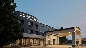Un hôtel Courtyard by Marriott au design moderne, doté d’une entrée couverte et d’un espace paysager aménagé avec des sièges.