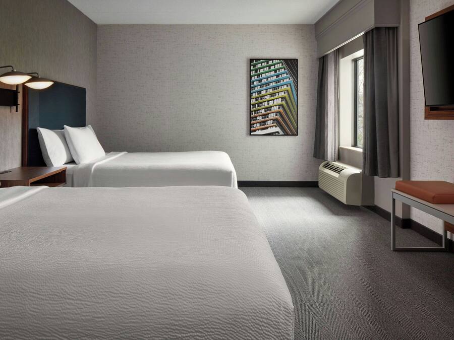 Une chambre d’hôtel avec deux lits, une grande fenêtre avec des rideaux, un téléviseur fixé au mur et un radiateur.