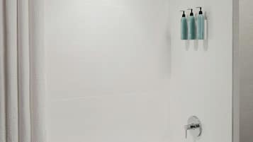 A modern bathroom with a white bathtub, a showerhead, and a towel rack with bottles.