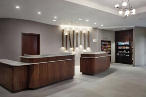 A reception area with two wooden reception desks, a wall-mounted sign reading "Market", and a refrigerator stocked with beverages.