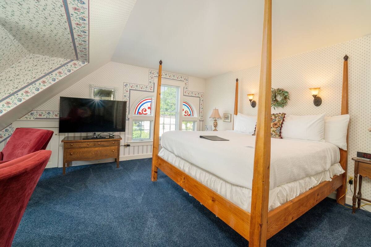 A bedroom with a four-poster bed, a television, a red chair, and a wooden nightstand.