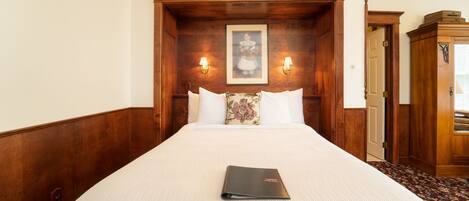 Une chambre d’hôtel avec un grand lit, une tête de lit en bois, deux lampes fixées au mur et un tableau encadré au-dessus du lit.