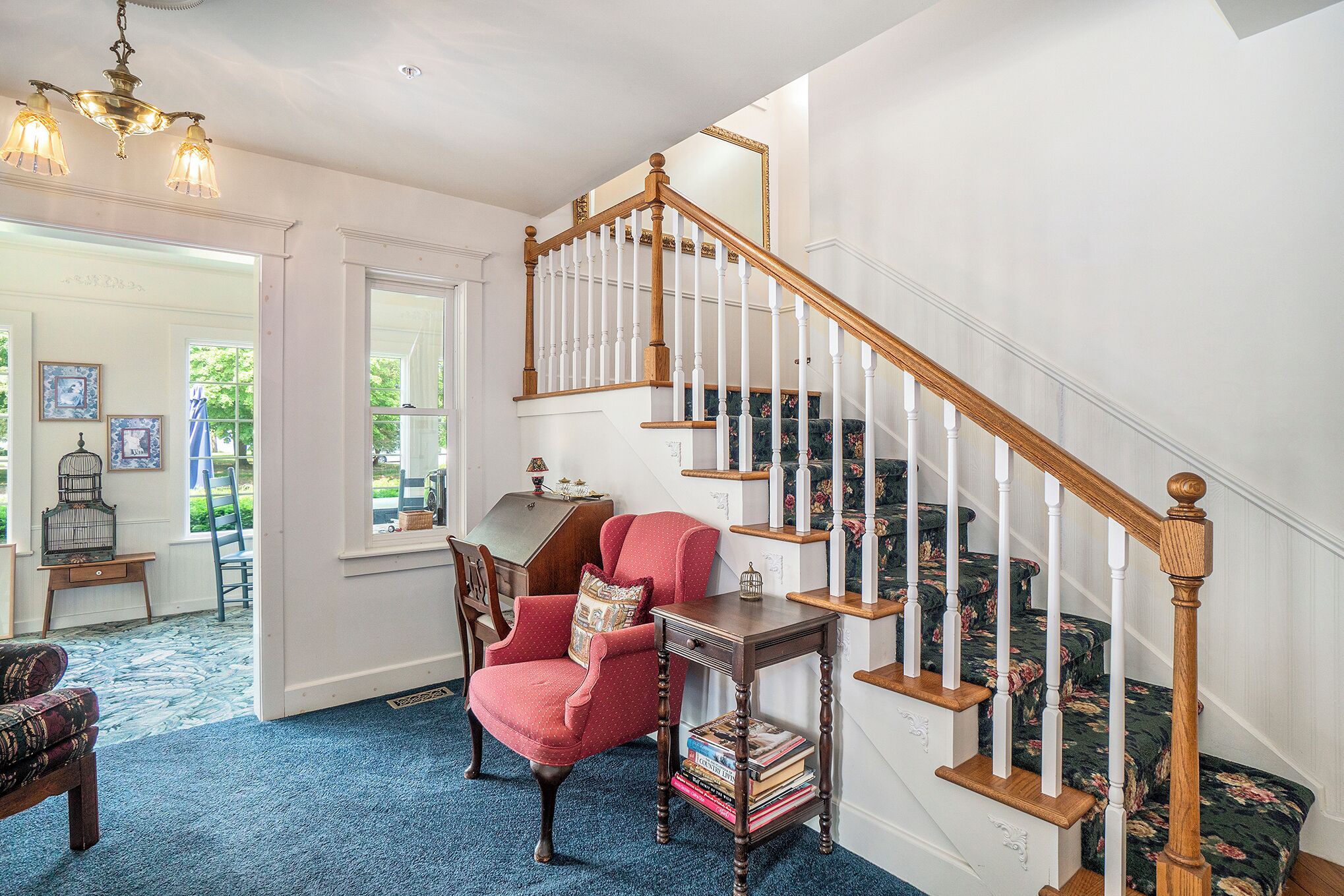 Un escalier avec des balustrades en bois et un fauteuil rouge recouvert de tissu, agrémenté d’un coussin.