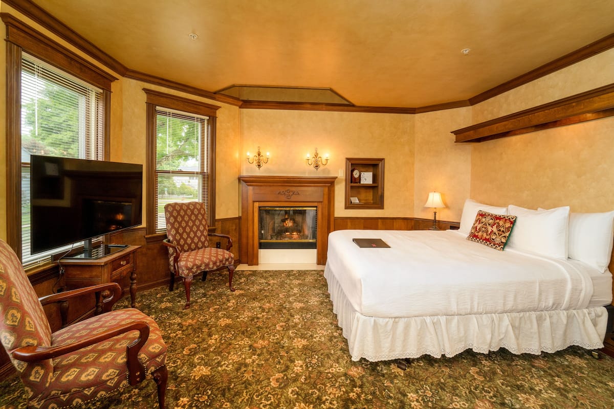 A hotel room with a large bed, a television, a fireplace, and a carpeted floor.