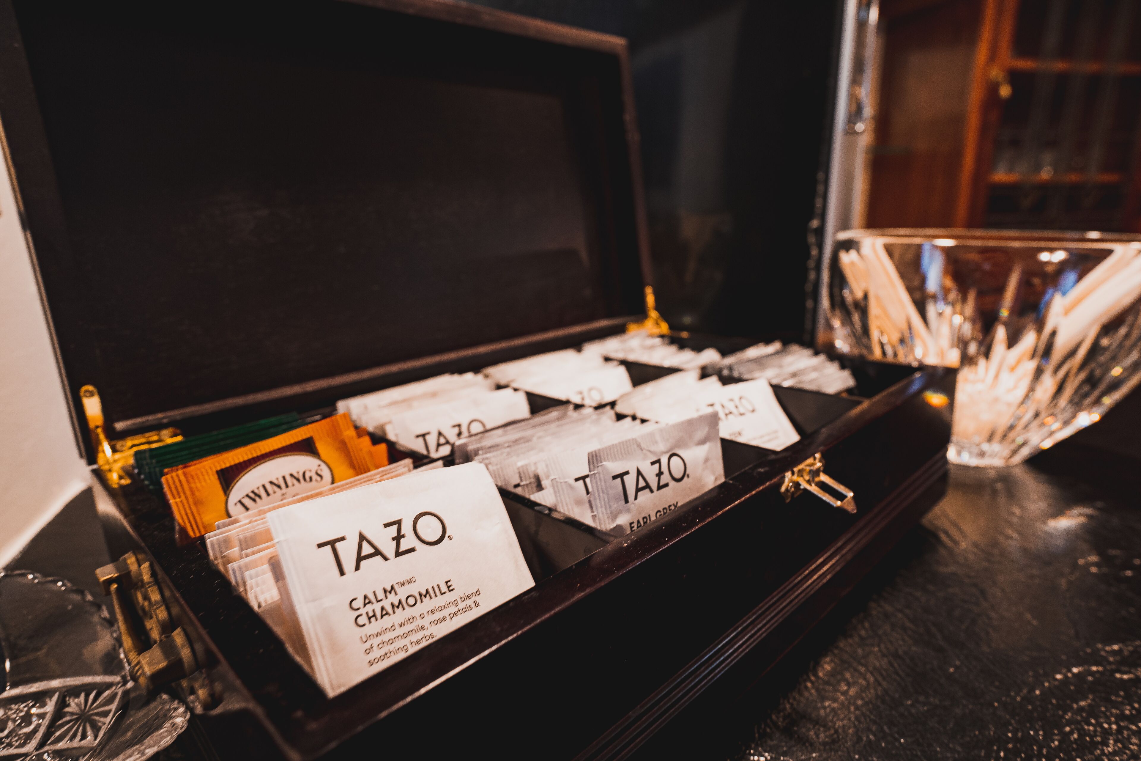 Une boîte noire comportant des compartiments contenant différents sachets de thé de marques connues, étiquetés « TAZO » et « TWININGS ».