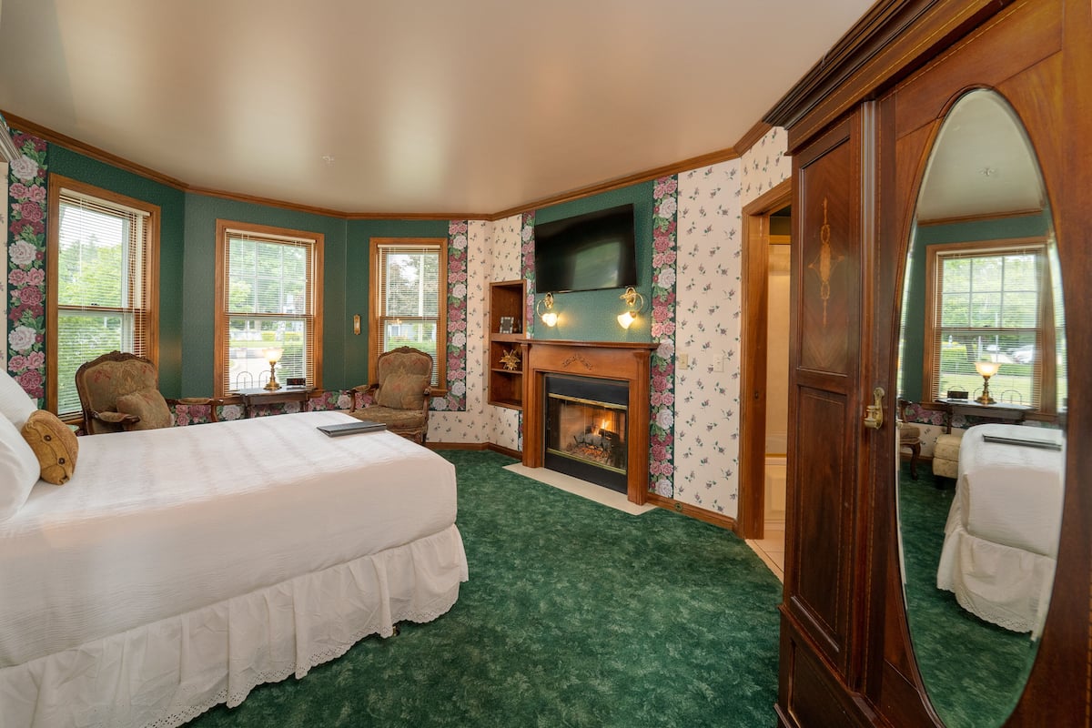 A bedroom with a large bed, a fireplace, a television, and floral wallpaper.