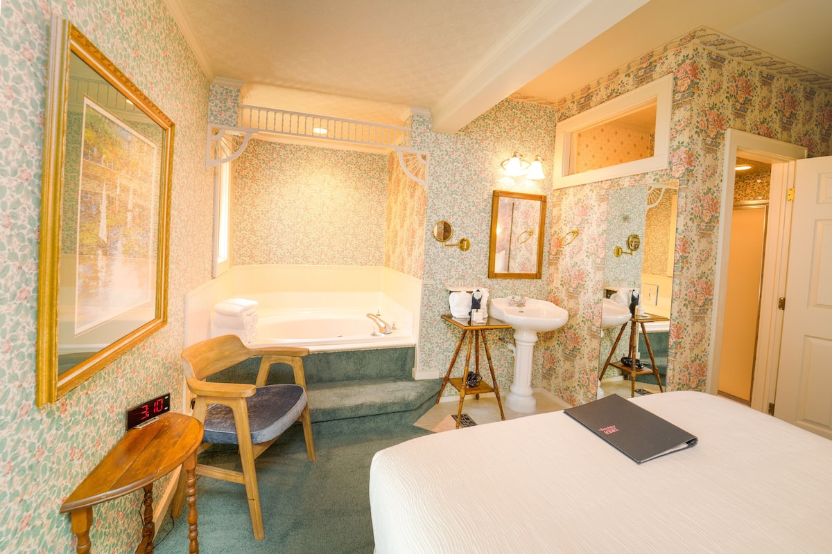 A hotel room with a bed, a chair, a small table, a sink, and a bathtub.