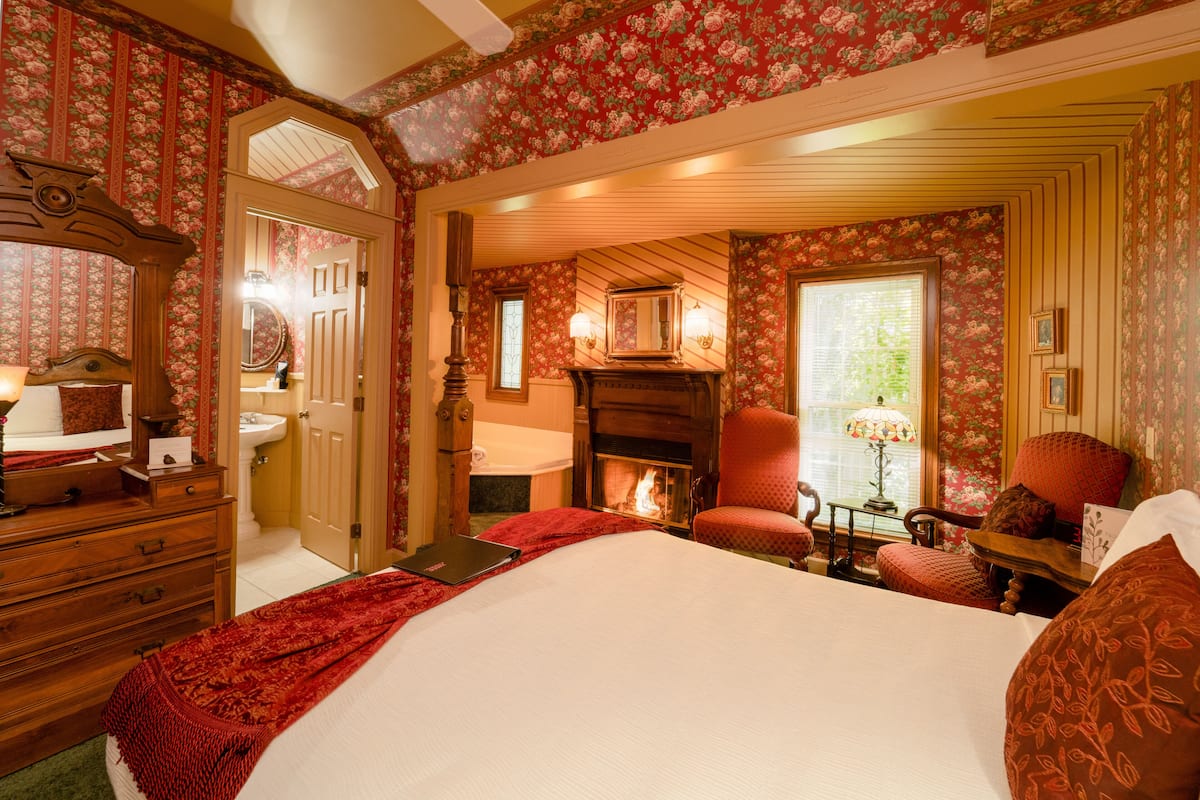 A traditional bedroom with a fireplace, a bed, a dresser, and a mirror.