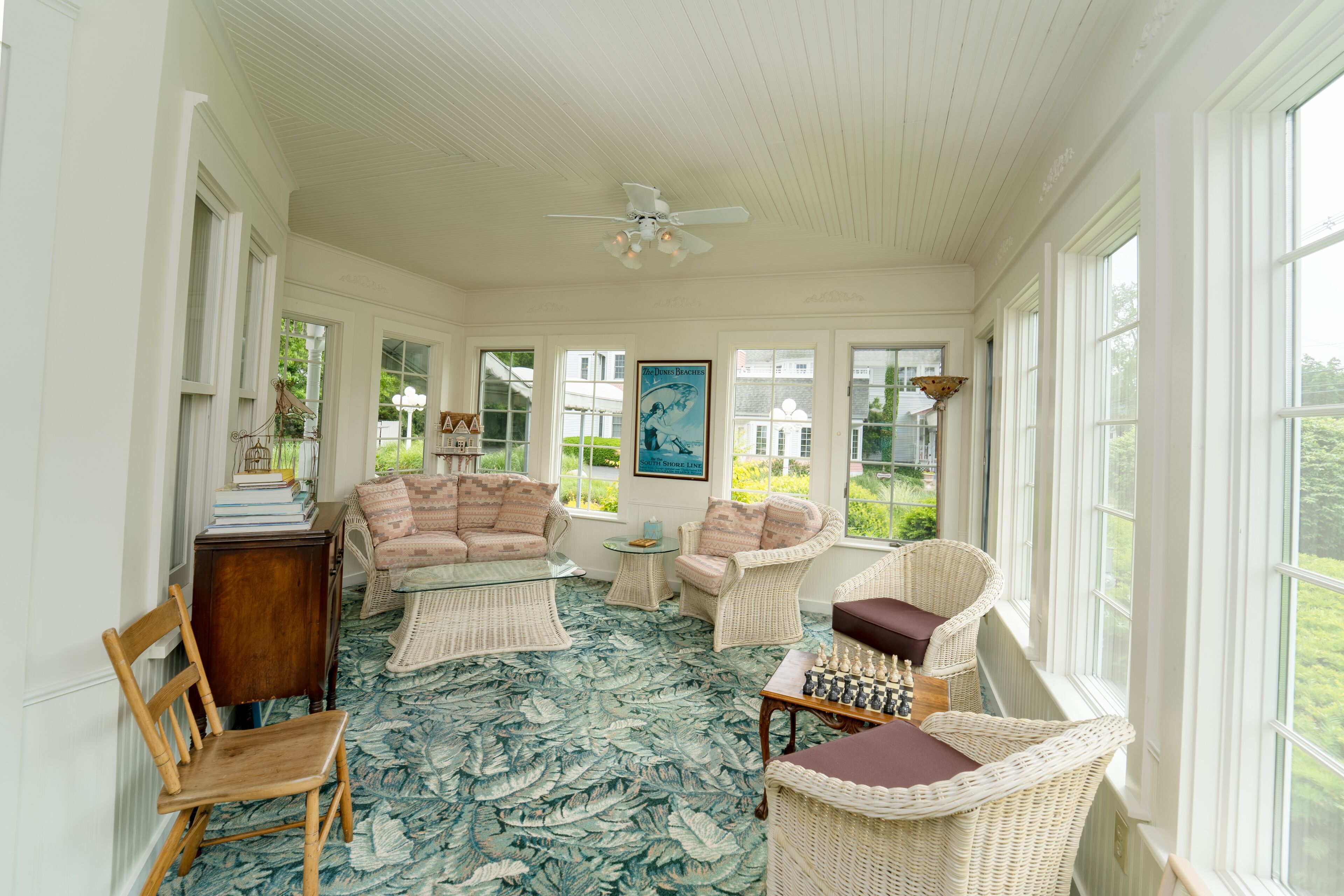 A sunroom with wicker furniture, a chessboard, and a view of greenery outside.