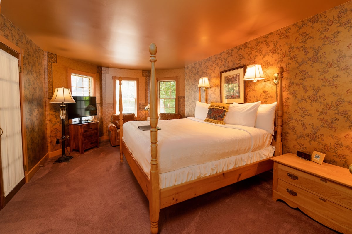 A four-poster bed with a wooden frame, a bedside table with a lamp, and a nightstand with a clock.