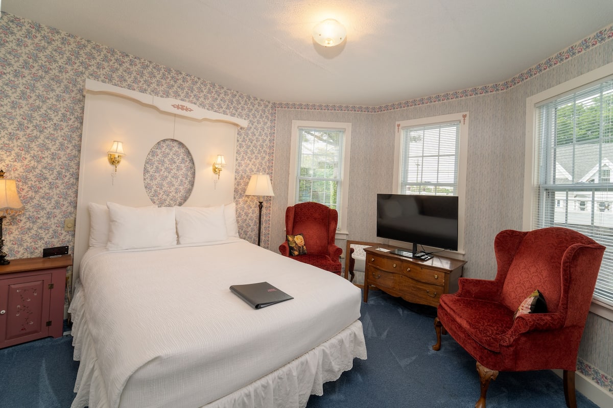 A bedroom with a large bed, a TV, a red armchair, and a dresser.
