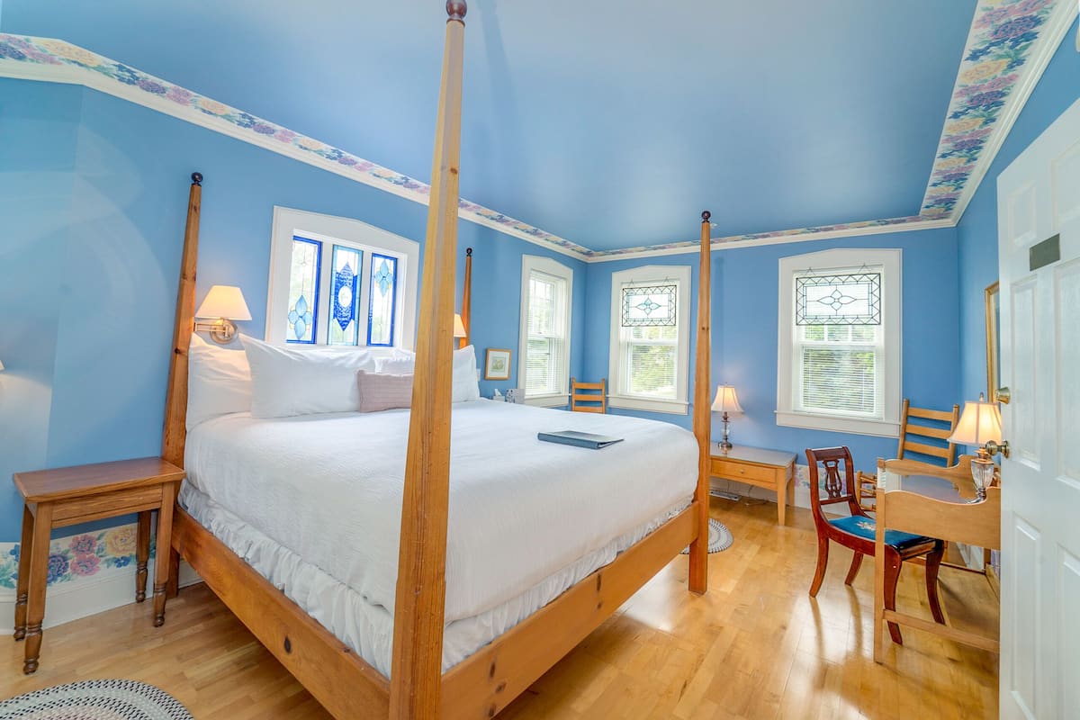 A four-poster bed with white linens, wooden nightstands, and a wooden chair with a cushion.